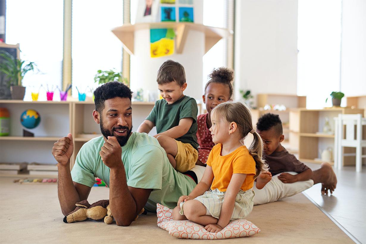 Group of small nursery school children with man teacher sitting on floor indoors in classroom, 玩.